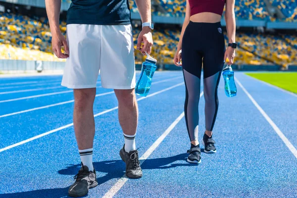 Tiro recortado de pareja deportiva con botellas de agua en pista de atletismo en el estadio deportivo - foto de stock