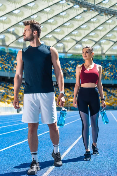 Молода спортивна пара з пляшками води, що розслабляються на біговій доріжці на спортивному стадіоні — стокове фото