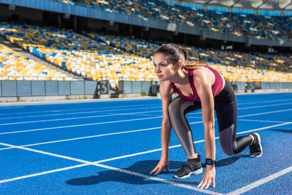 Corredor femenino en forma en posición de inicio en pista de atletismo en el estadio deportivo - foto de stock