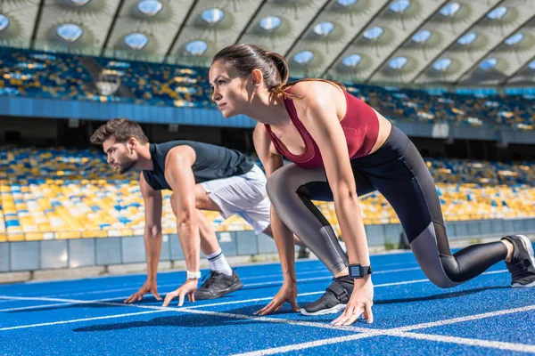Sportive young male and female sprinters in start position on running track at sports stadium — Stock Photo
