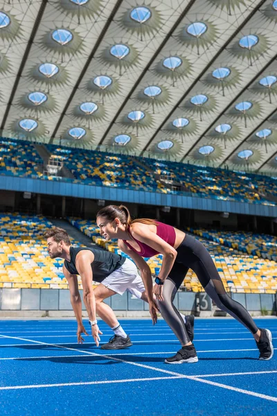Caben jóvenes velocistas masculinos y femeninos en posición de inicio en pista de atletismo en el estadio deportivo - foto de stock