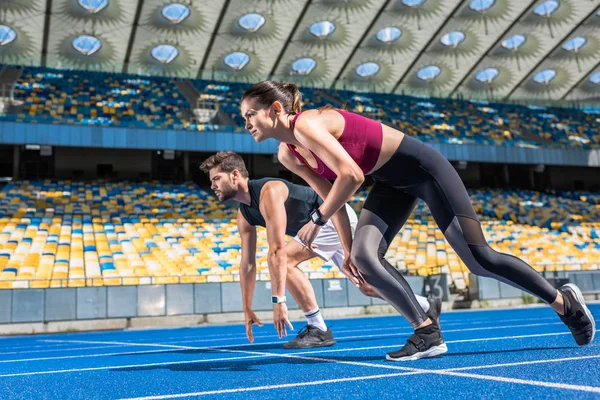 Atléticos jóvenes velocistas masculinos y femeninos en posición de inicio en pista de atletismo en el estadio deportivo - foto de stock