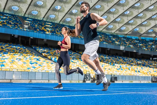 Plan de mouvement de jeunes joggeurs masculins et féminins qui courent sur la piste au stade de sport — Photo de stock