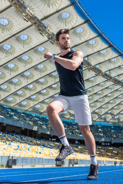 Vista inferior del joven atlético haciendo ejercicio en pista de atletismo en el estadio deportivo - foto de stock
