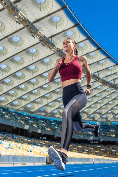 Vista inferior de la atractiva joven corriendo en pista en el estadio deportivo - foto de stock