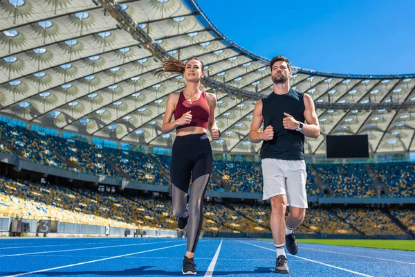 Vista inferior de joggers jóvenes masculinos y femeninos corriendo en pista en el estadio deportivo - foto de stock