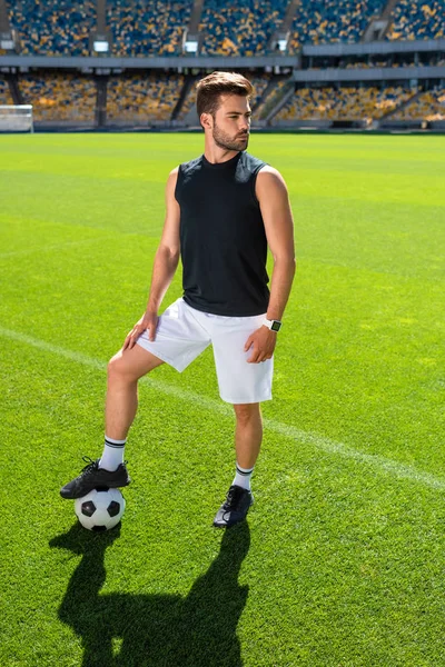 Серйозний молодий футболіст, що стоїть на спортивному стадіоні з м'ячем — стокове фото