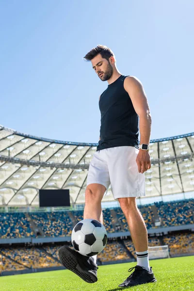 Apuesto joven futbolista haciendo ejercicio con pelota en el estadio deportivo - foto de stock