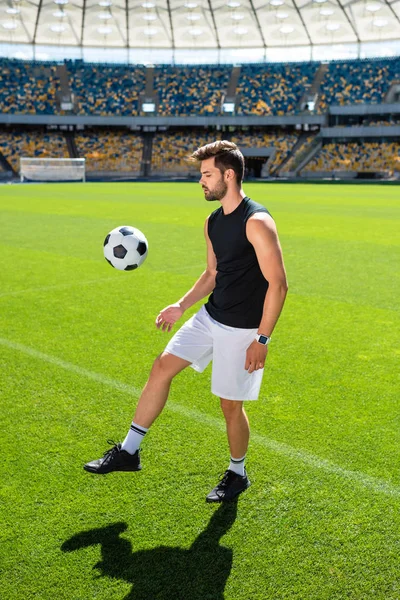 Attrayant jeune joueur de football rebondissant ballon sur la jambe au stade de sport — Photo de stock