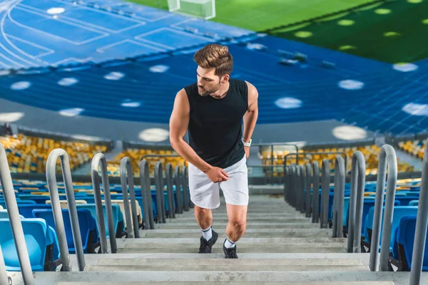 Vista de ángulo alto del joven deportivo corriendo arriba en el estadio de deportes - foto de stock
