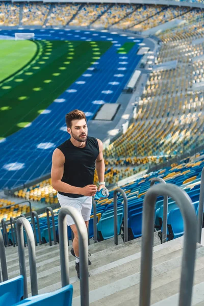Vista de ángulo alto de joven guapo corriendo arriba en el estadio de deportes - foto de stock