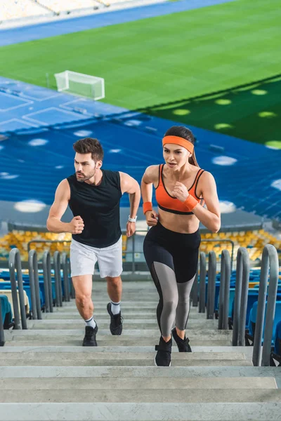 Vista de ángulo alto de la joven pareja deportiva corriendo arriba en el estadio deportivo - foto de stock
