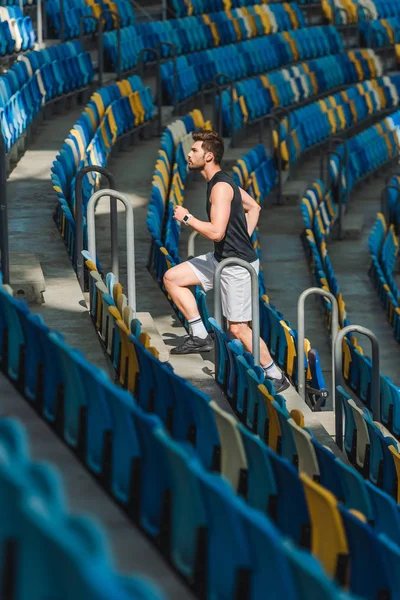 Side view of attractive young man jogging upstairs at sports stadium — Stock Photo