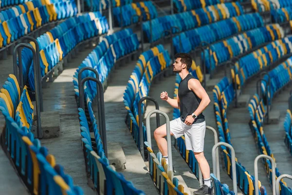 Vista lateral del joven guapo corriendo arriba en el estadio deportivo - foto de stock