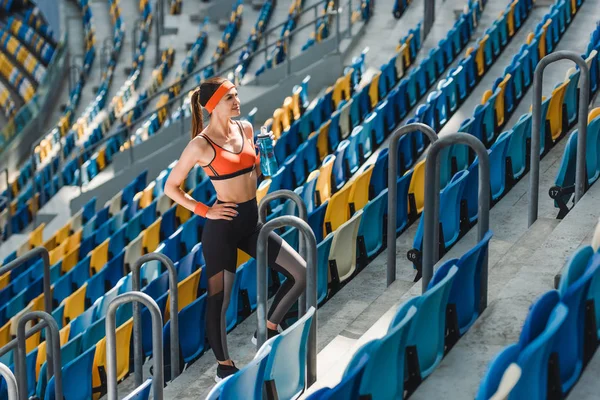 Высокий угол зрения на красивую молодую женщину, стоящую на лестнице на спортивном стадионе и смотрящую в сторону — стоковое фото