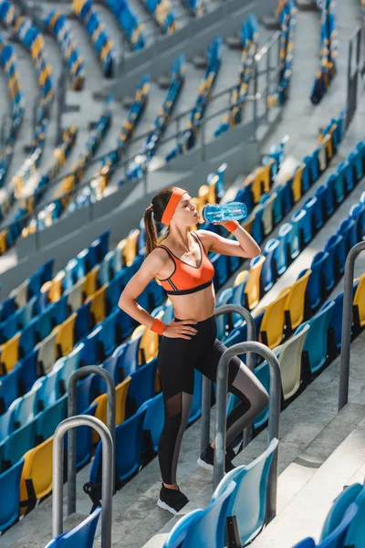 Visão de alto ângulo de feliz jovem mulher bebendo água em tribunos no estádio de esportes — Fotografia de Stock