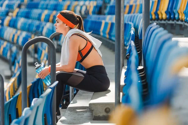 Vista laterale della giovane donna stanca con acqua seduta sulle scale dello stadio sportivo — Foto stock