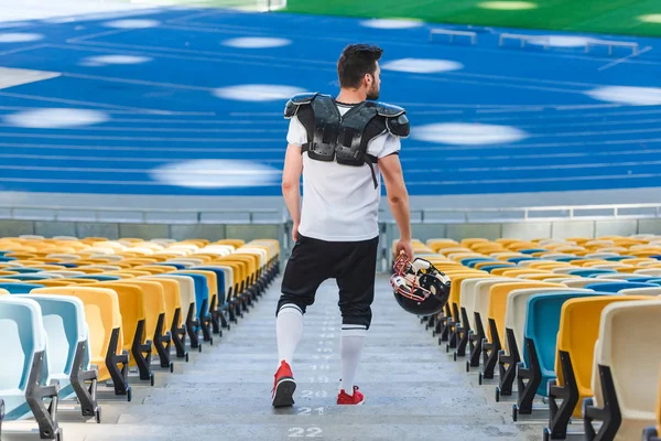 Vista trasera del joven jugador de fútbol americano en las escaleras en el estadio deportivo - foto de stock