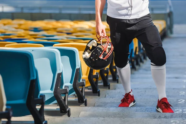 Recortado tiro de jugador de fútbol americano con casco de pie en las escaleras en el estadio de deportes - foto de stock
