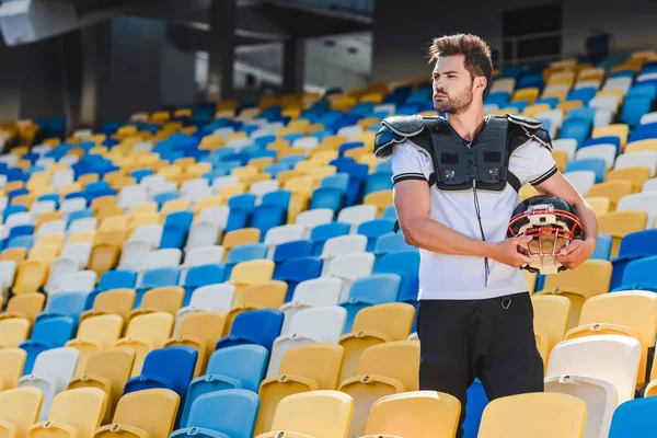 Bonito jovem jogador de futebol americano em equipamentos de pé sobre tribunos no estádio de esportes — Fotografia de Stock
