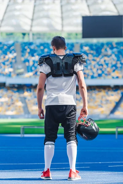 Вид сзади на американского футболиста в шлеме, стоящего в одиночестве на спортивном стадионе — стоковое фото