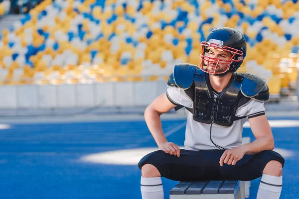 Beau jeune footballeur américain assis sur le banc au stade de sport — Photo de stock