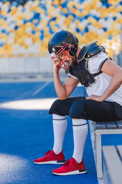 Deprimido joven jugador de fútbol americano sentado en el estadio de deportes - foto de stock