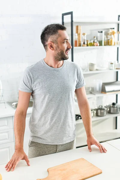 Вид сбоку взрослого мужчины, стоящего возле стола с разделочной доской на кухне — стоковое фото