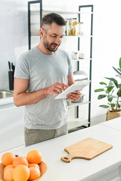 Hombre feliz usando tableta digital cerca de la mesa en la cocina - foto de stock