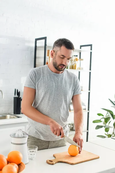 Focado homem adulto cortando laranja por faca na cozinha — Fotografia de Stock