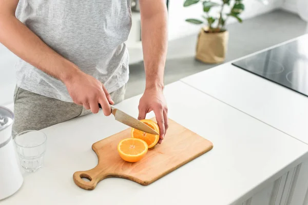 Cropped image of man cutting oranges by knife on tabletop — Stock Photo