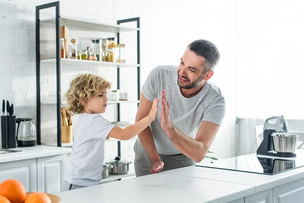 Feliz hombre adulto dando alta cinco a pequeño hijo en la cocina - foto de stock