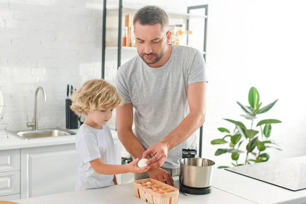 Father giving egg to little son near tabletop at kitchen — Stock Photo