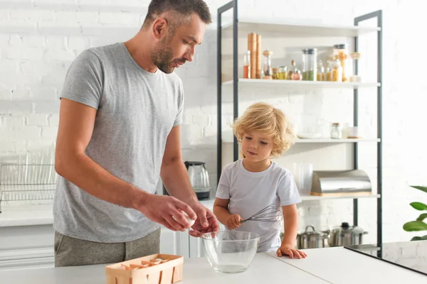 Père avec oeuf et fils avec fouet se préparant à faire de la pâte à la cuisine — Photo de stock