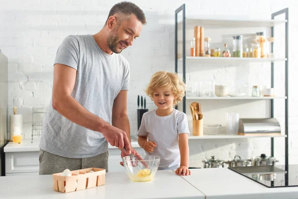 Père et fils fouettant des œufs dans un bol sur la table à la cuisine — Photo de stock