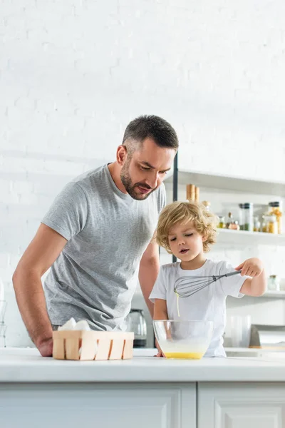 Padre con hijo batiendo huevos en un tazón en la cocina - foto de stock