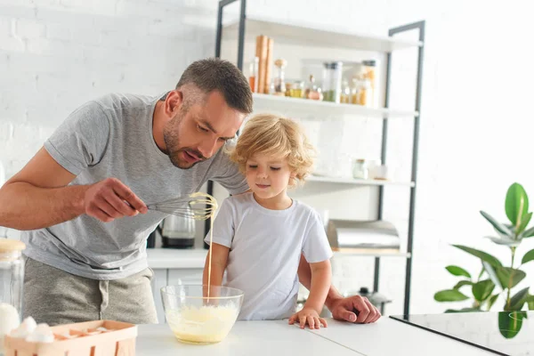 Человек учит сына делать тесто в миске на кухне — стоковое фото