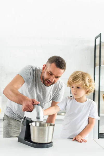 Vater lehrt Sohn mit Mixer auf Tischplatte in Küche — Stockfoto