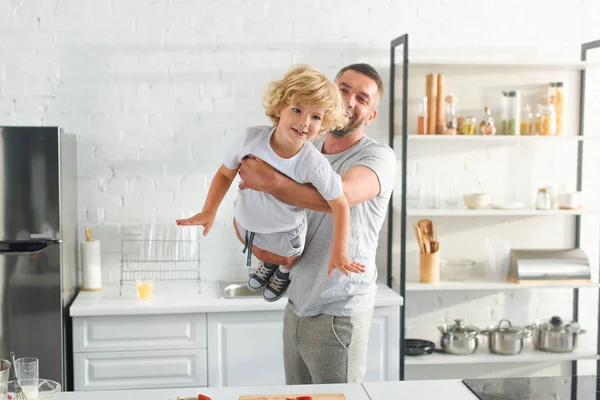 Отец воспитывает улыбающегося маленького сына на кухне — стоковое фото