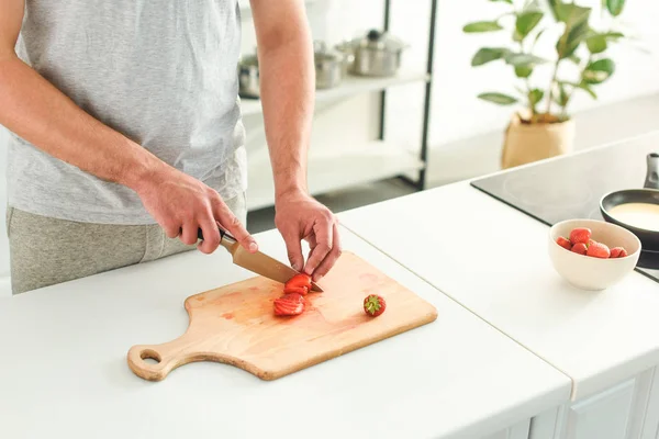 Cropped image of man cutting strawberry by knife on table at kitchen — Stock Photo