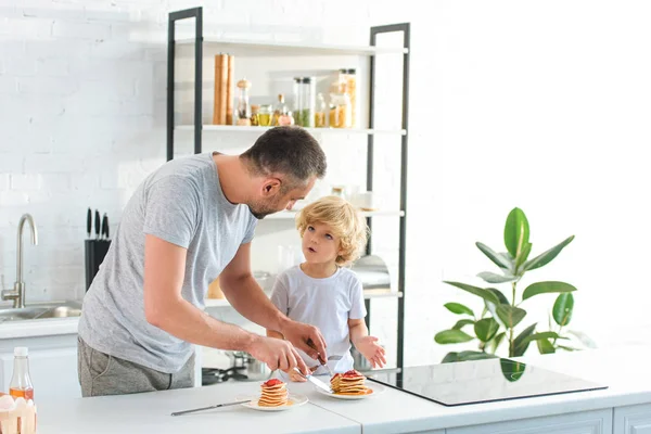 Padre tagliare frittelle e parlare con il piccolo figlio in cucina — Foto stock