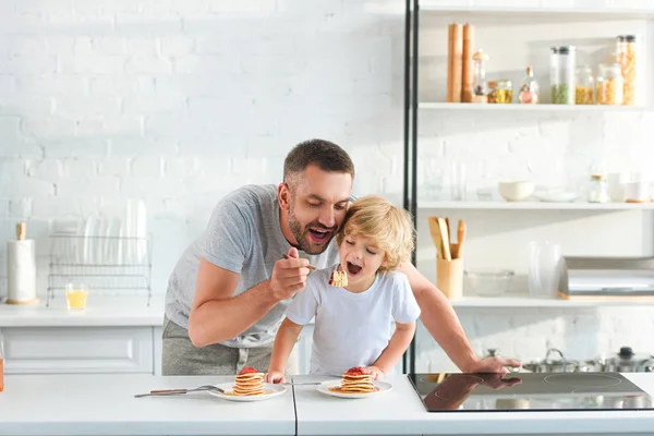 Glücklicher Vater und Sohn essen Pfannkuchen in der Küche — Stockfoto