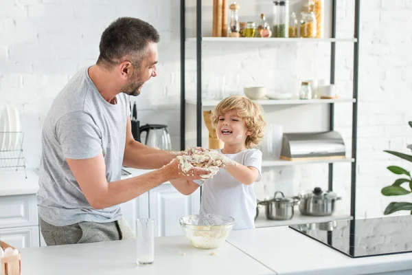 Pai feliz e filho se divertindo ao fazer massa na tigela na cozinha — Fotografia de Stock