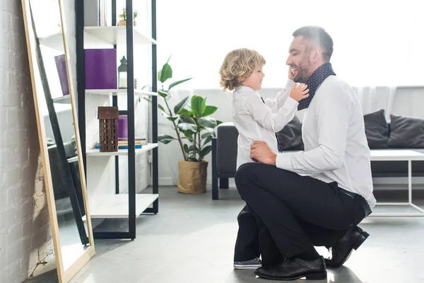 Vista lateral del niño ayudando al padre a atar la corbata en casa - foto de stock