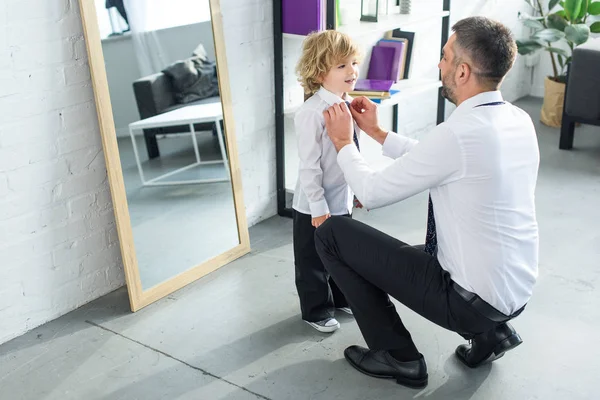 Rear view of father helping son tying necktie at home — Stock Photo