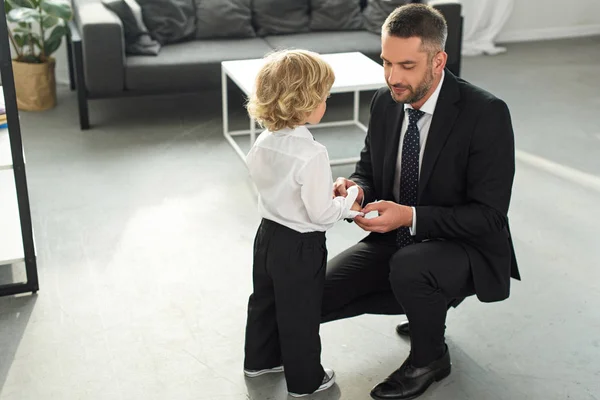 Adult man in suit fastening buttons on shirt sleeve of son — Stock Photo