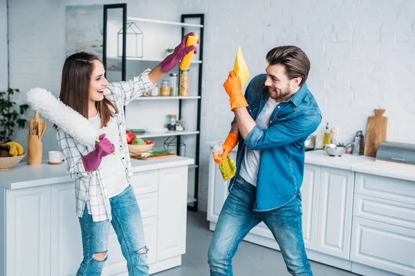 Casal se divertindo durante a limpeza da cozinha e lutando com ferramentas de limpeza — Fotografia de Stock