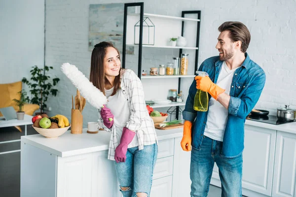 Couple having fun with spray bottle and dust brush during cleaning kitchen — Stock Photo