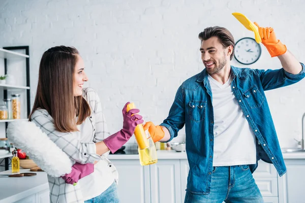 Fidanzato e fidanzata divertirsi durante la pulizia della cucina e combattere con strumenti di pulizia — Foto stock