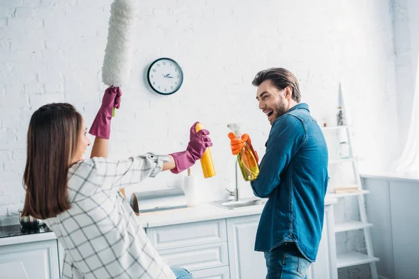 Casal feliz se divertindo durante a limpeza da cozinha e lutando com ferramentas de limpeza — Fotografia de Stock